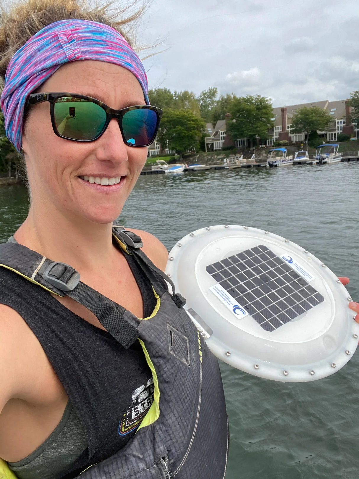 Woman holding lake water testing device with solar panel near shoreline homes for Lake Pulse.